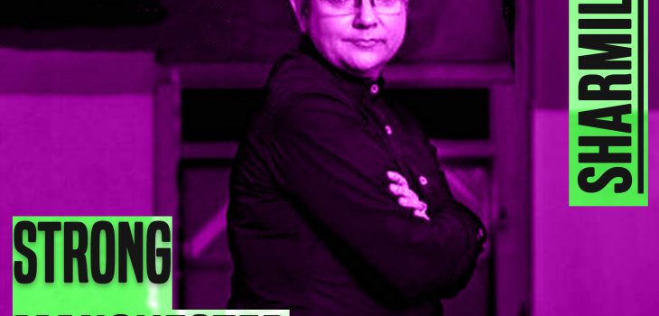 a photo of a woman who is sat down. The photo shows her from her knees up. She has short hair and wears glasses. Her arms are folder and she is looking directly at the camera. The image has a purple tinge. On the left of the seated woman are the words 'strong manchester women' and to the top right of the woman are the words 'Sharmila Kar' Both sets of words are in bold grey type.