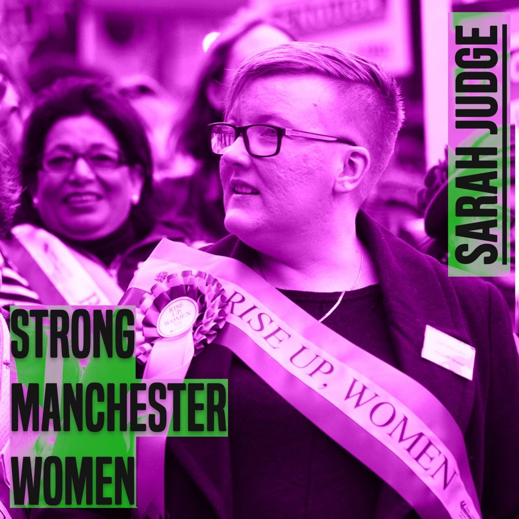 The picture is a of a woman from chest height up. She has her head turned to the left. She has short hair and glasses. she is wearing a sash. She The picture has a purple hue to it. On the leff of the picture are the words 'strong manchester women' on the right 'Sarah Judge' - both in capital and grey colour letters