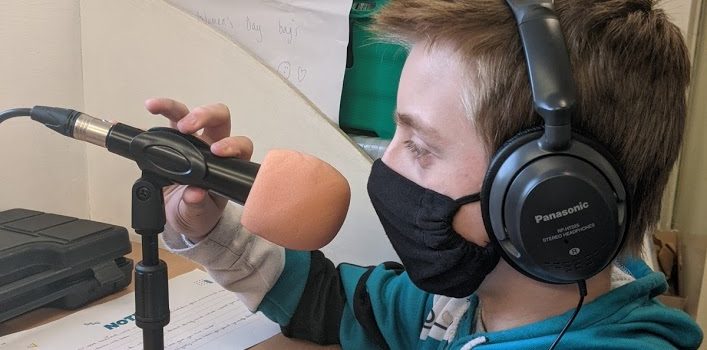 Image of a boy with headphones and a face mask on holding a microphone on a stand
