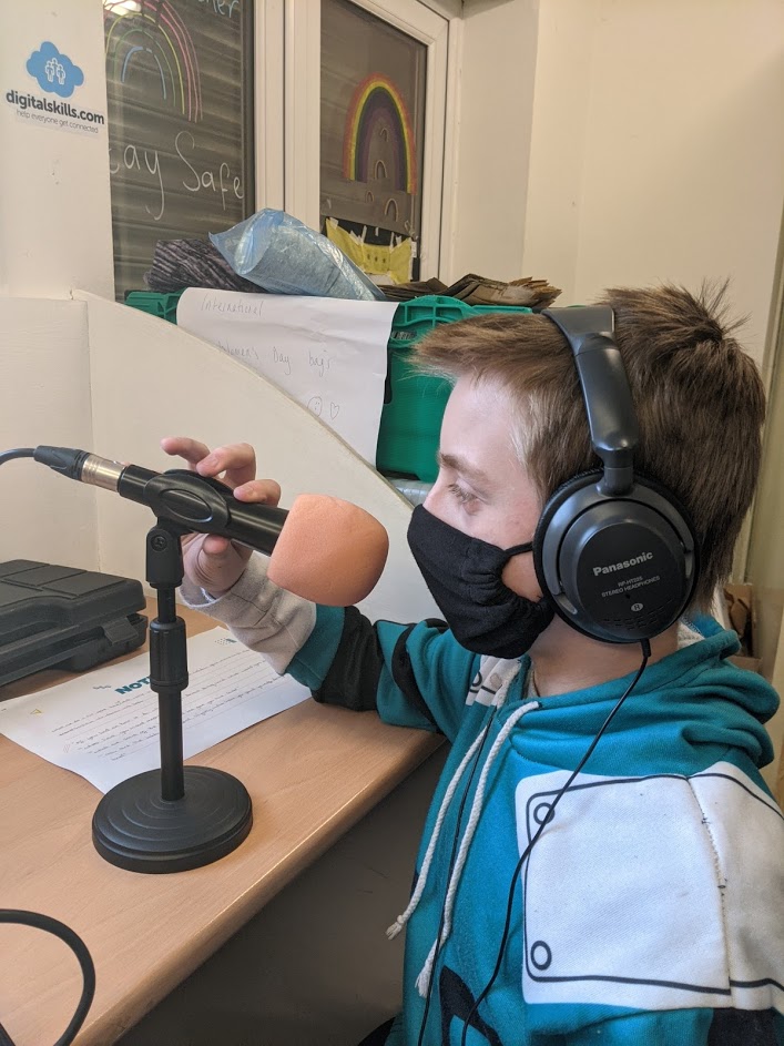 Image of a boy with headphones and a face mask on holding a microphone on a stand